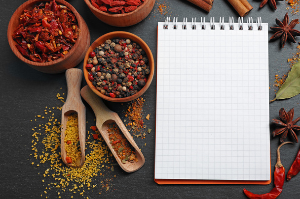 Assorted spices with recipe notebook on black table background - Foto, afbeelding