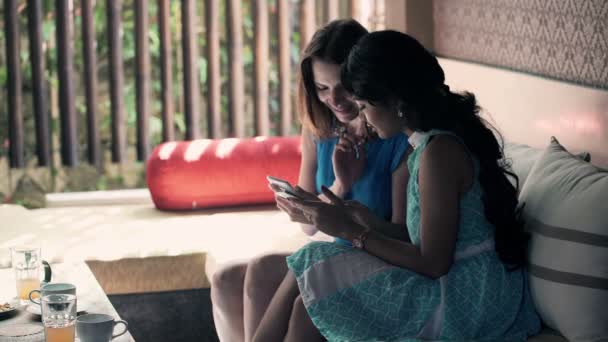 girlfriends talking and using smartphone sitting on sofa - Materiaali, video