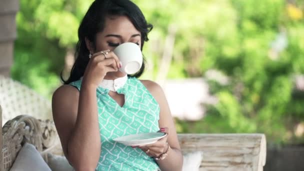 woman drinking coffee sitting on sofa on terrace - Кадри, відео