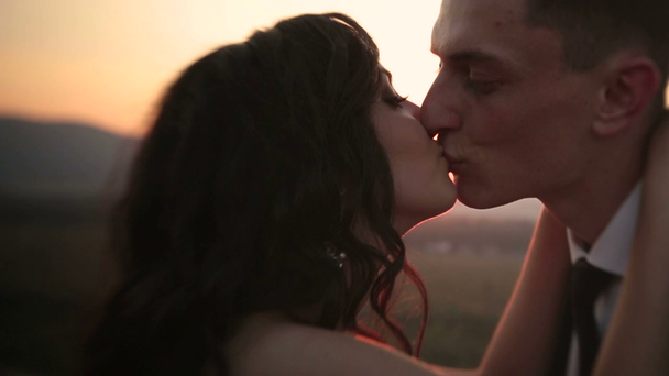 Piękna brunetka narzeczeni całowanie na zachód słońca z bliska - Materiał filmowy, wideo