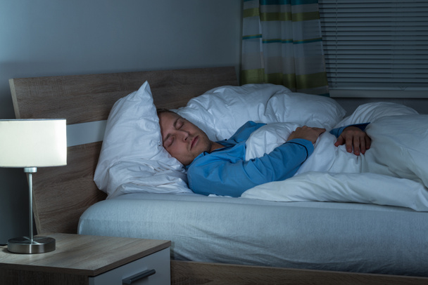 Νεαρός άνδρας που κοιμάται στο υπνοδωμάτιό - Φωτογραφία, εικόνα