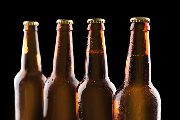 Four bottles of beer on black background - Фото, изображение