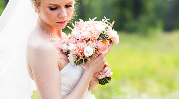 Beautiful bride with wedding bouquet of flowers outdoors in green park. - Foto, imagen