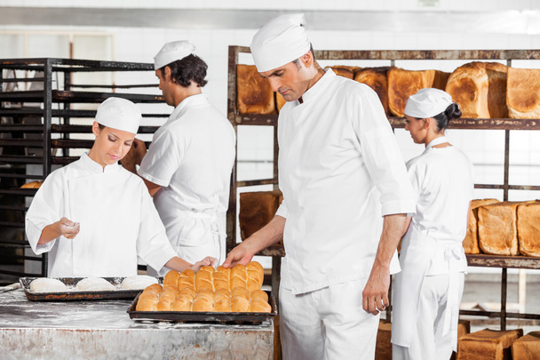 Baker Analyzing Breads While Colleagues Working In Bakery - Foto, Imagen