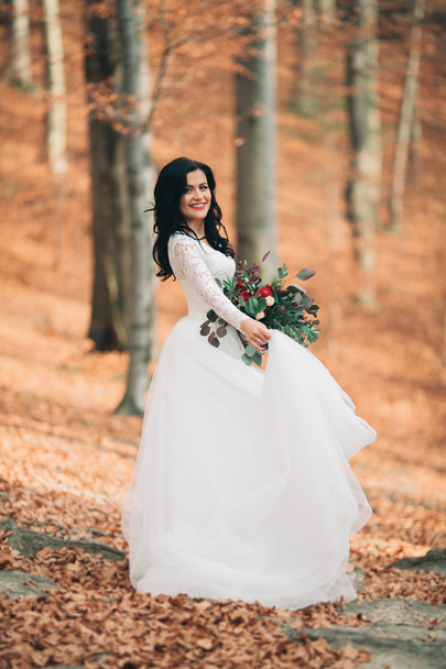 Gorgeous brunette bride in elegant dress holding bouquet  posing near forest and lake - Fotoğraf, Görsel