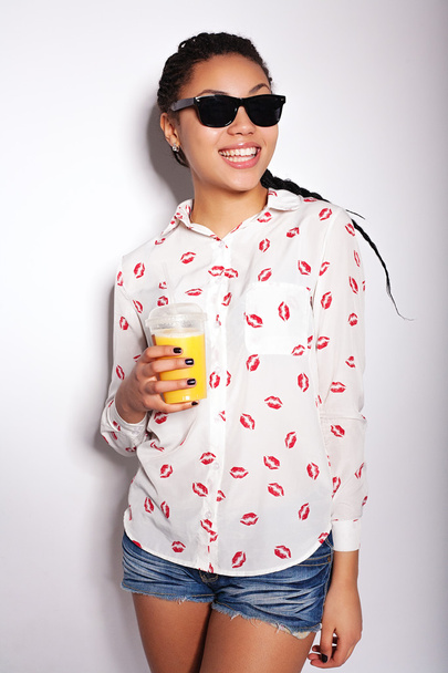 Όμορφη νεαρή κοπέλα ποζάρει στο studio σε λευκό φόντο. Πίνοντας χυμό πορτοκαλιού - Φωτογραφία, εικόνα
