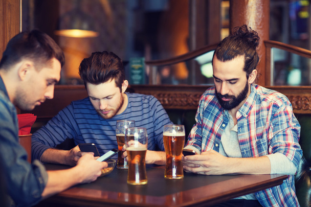 male friends with smartphones drinking beer at bar - Fotografie, Obrázek