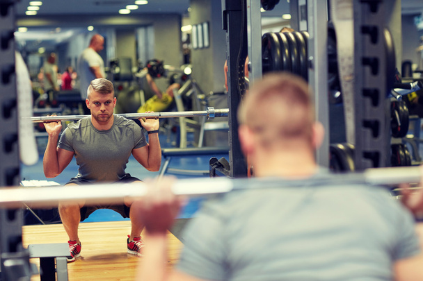 joven hombre flexionando los músculos con barra en el gimnasio - Foto, imagen
