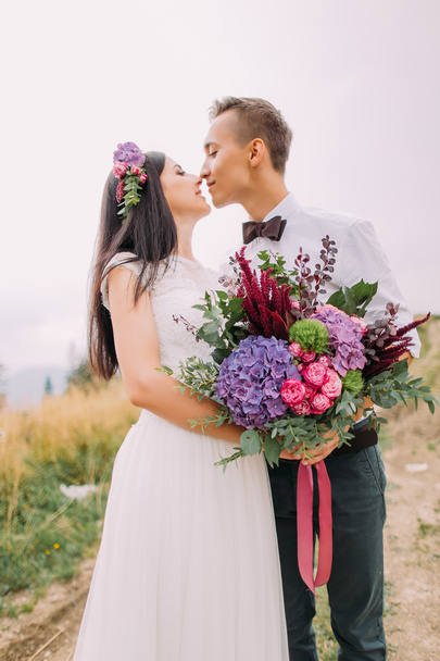 Happy bride and groom kiss with bouquet in hands close up - Foto, Imagem