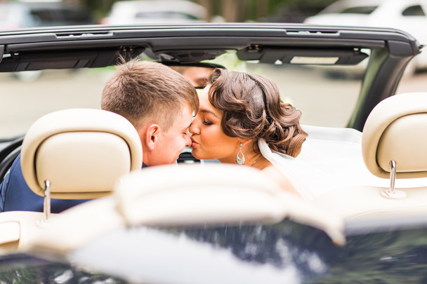 Mooie jonge paar bruid en bruidegom poseren in cabriolet - Foto, afbeelding