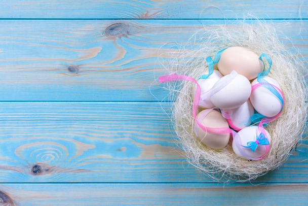 Huevos de Pascua con cintas de colores y arco en el nido sobre fondo de madera azul. Vista superior con etiqueta para espacio de copia
 - Foto, Imagen