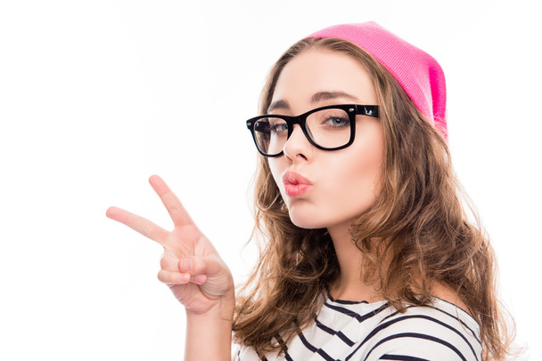  smiling girl in hat and glasses showing two fingers and pouting - Foto, Imagen