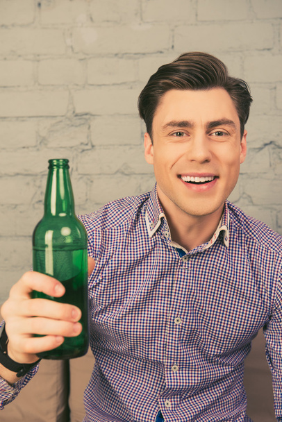 Portrait of happy man sitting on sofa with bottle of beer - Zdjęcie, obraz