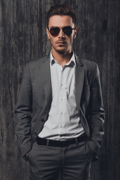 Stylish confident man holding hands in pockets on the grey backg - Fotó, kép