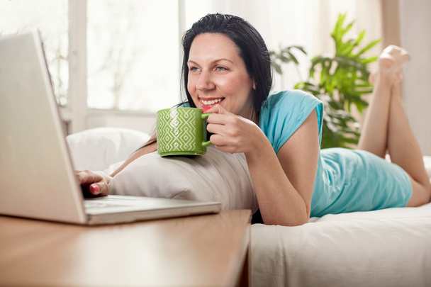 schöne junge Frau, die mit einer Tasse Kaffee im Bett liegt  - Foto, Bild
