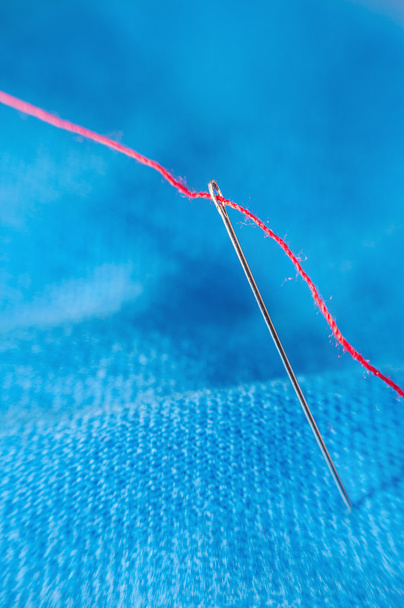 Macro red thread through needle hole on blue blurred background - Photo, Image