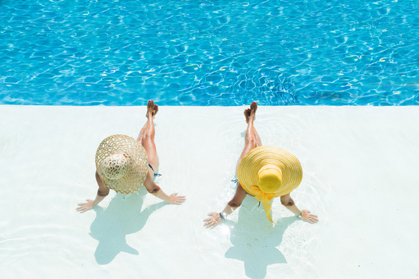 Two women in a hat sitting on the edge of the pool - Fotografie, Obrázek