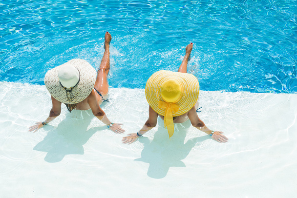 Two women in a hat sitting on the edge of the pool - Photo, Image