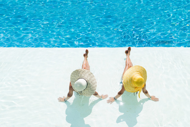 Two women in a hat sitting on the edge of the pool - Foto, imagen