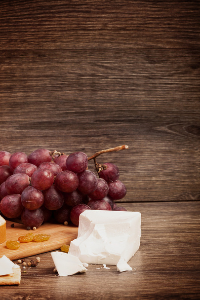 weißer Käse, Nüsse und rote Trauben auf Holzgrund - Foto, Bild