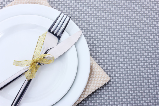 White empty plates with fork and knife tied with a ribbon on a grey tablecloth - Fotoğraf, Görsel