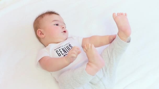 Kleine babyjongen spelen met zijn voeten tegen witte achtergrond - Video
