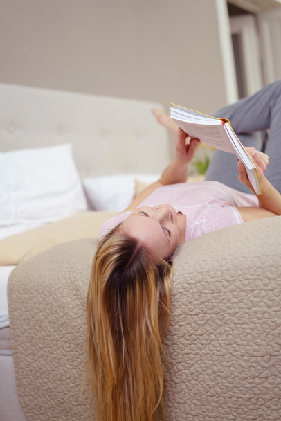 Mujer joven relajándose leyendo un libro en una cama
 - Foto, Imagen