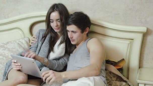 Young couple lying on the bed make shopping over the Internet using tablet - Кадри, відео