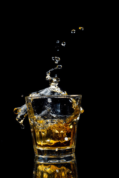 Whiskey splash in glass isolated on black background. - Foto, afbeelding