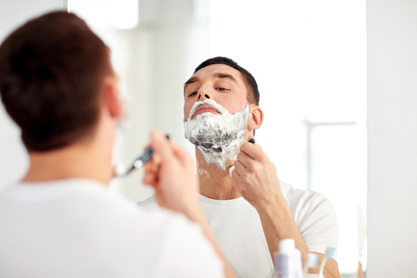 man shaving beard with razor blade at bathroom - Foto, afbeelding