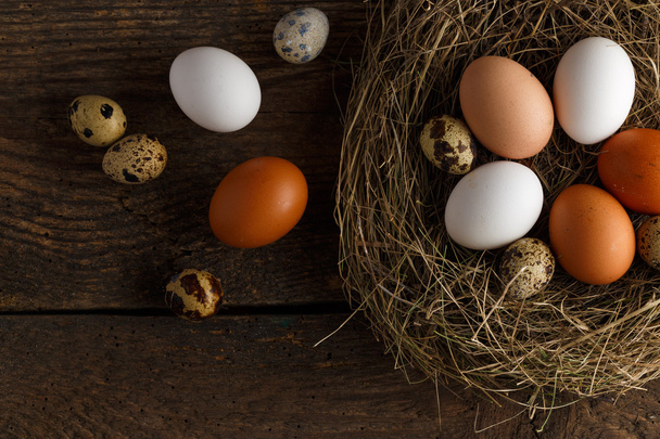 Chicken and quail eggs in a nest on a wooden rustic background - Photo, Image