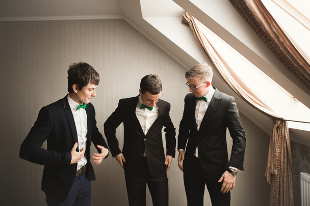 Happy friends helps stylish groom getting ready for his wedding day - Foto, afbeelding