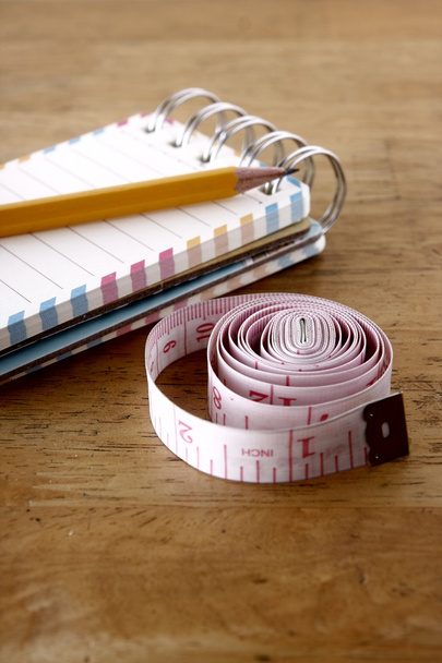 Piccolo quaderno a spirale colorato, matita e nastro di misurazione su un tavolo di legno
 - Foto, immagini