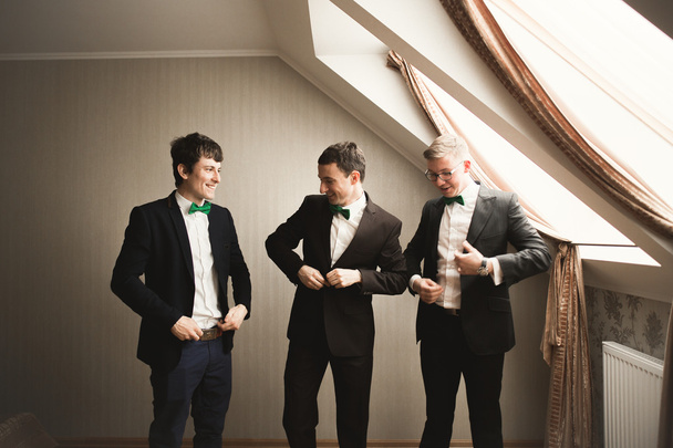 Happy friends helps stylish groom getting ready for his wedding day - Photo, image