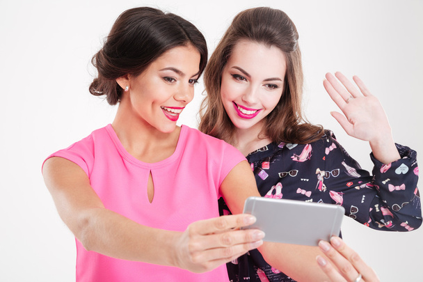 Two beautiful smiling young women making selfie using mobile phone - 写真・画像