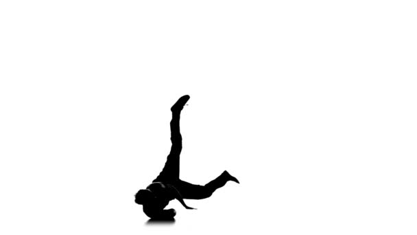 Muscular young man dancing breakdance on one hand, white, silhouette, slow motion - Záběry, video