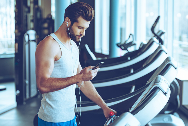 handsome man with phone on treadmill - Zdjęcie, obraz