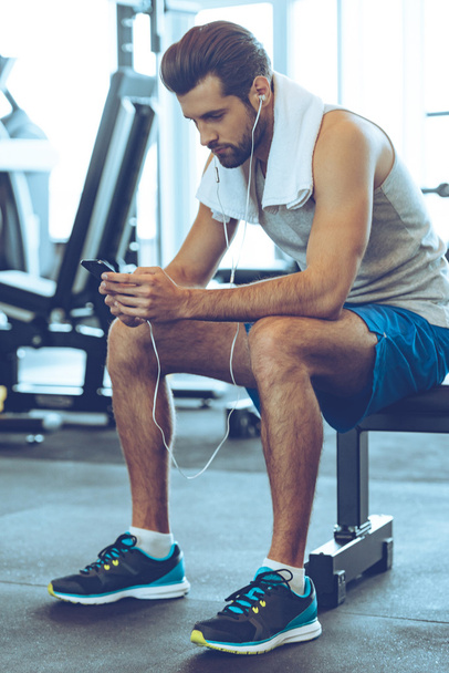 young man in headphones with phone at gym - Photo, Image