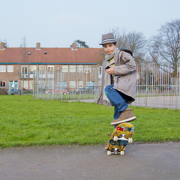 cute tiener met mobiele telefoon doen stunts op een skateboard - Foto, afbeelding