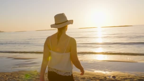 Όμορφη γυναίκα που περπατά σε μια παραλία κατά τη διάρκεια του ηλιοβασιλέματος - Πλάνα, βίντεο