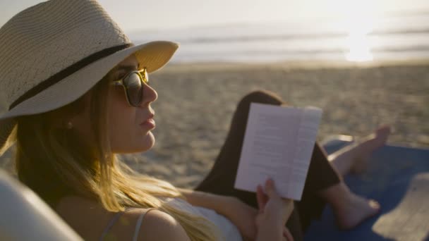 Piękna kobieta siedzi i czytania na plaży - Materiał filmowy, wideo