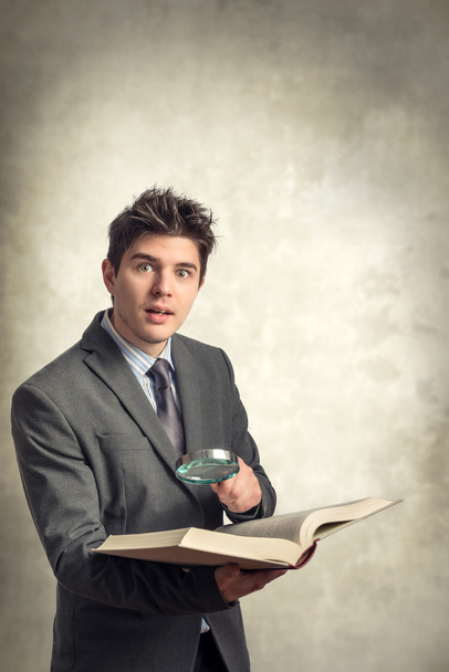 Jeune homme d'affaires regardant un livre avec loupe
 - Photo, image