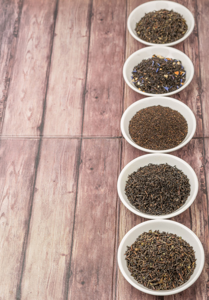 Feuilles de thé noir lâches et séchées variété dans des bols blancs sur fond en bois
 - Photo, image