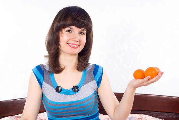 Beautiful girl sitting on the bed and keeps mandarins - Foto, Imagen