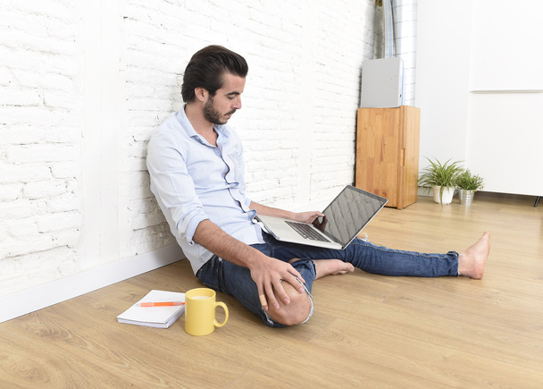 jovem no moderno estilo casual hipster olhar sentado na sala de estar chão em casa trabalhando no laptop
  - Foto, Imagem