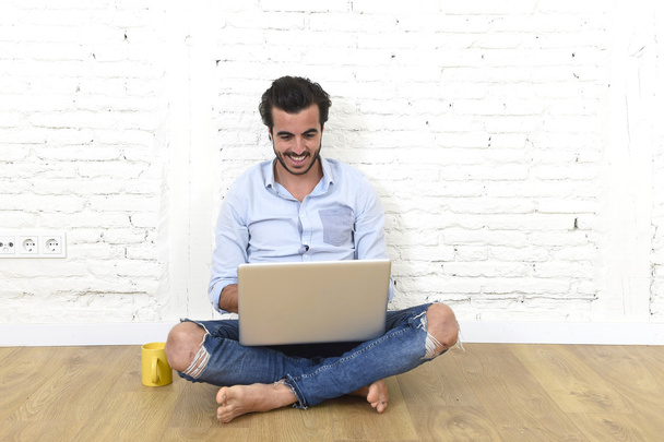 молодий чоловік в хіпстерському сучасному казуальному стилі виглядає, сидячи на підлозі будинку вітальні, працюючи на ноутбуці
  - Фото, зображення