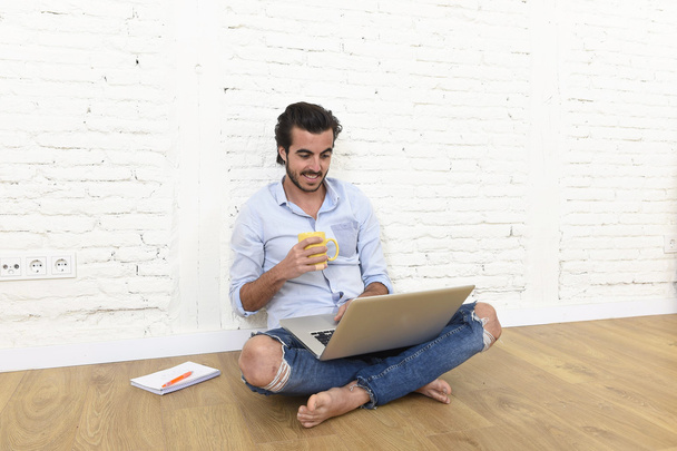 молодой человек в хипстерском стиле casual выглядит сидящим в гостиной на домашнем этаже, работающим на ноутбуке
  - Фото, изображение