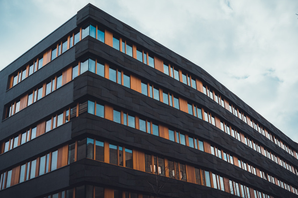 Baixo ângulo de vista de apartamento residencial com telhado plano edifício com fachada preta e janelas laranja emolduradas na Alemanha
 - Foto, Imagem
