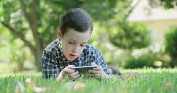 Junge spielt mit Handy auf dem Rasen - Filmmaterial, Video