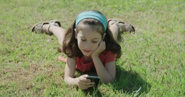 ein Mädchen spielt mit einem Handy, das auf dem Rasen liegt - Filmmaterial, Video
